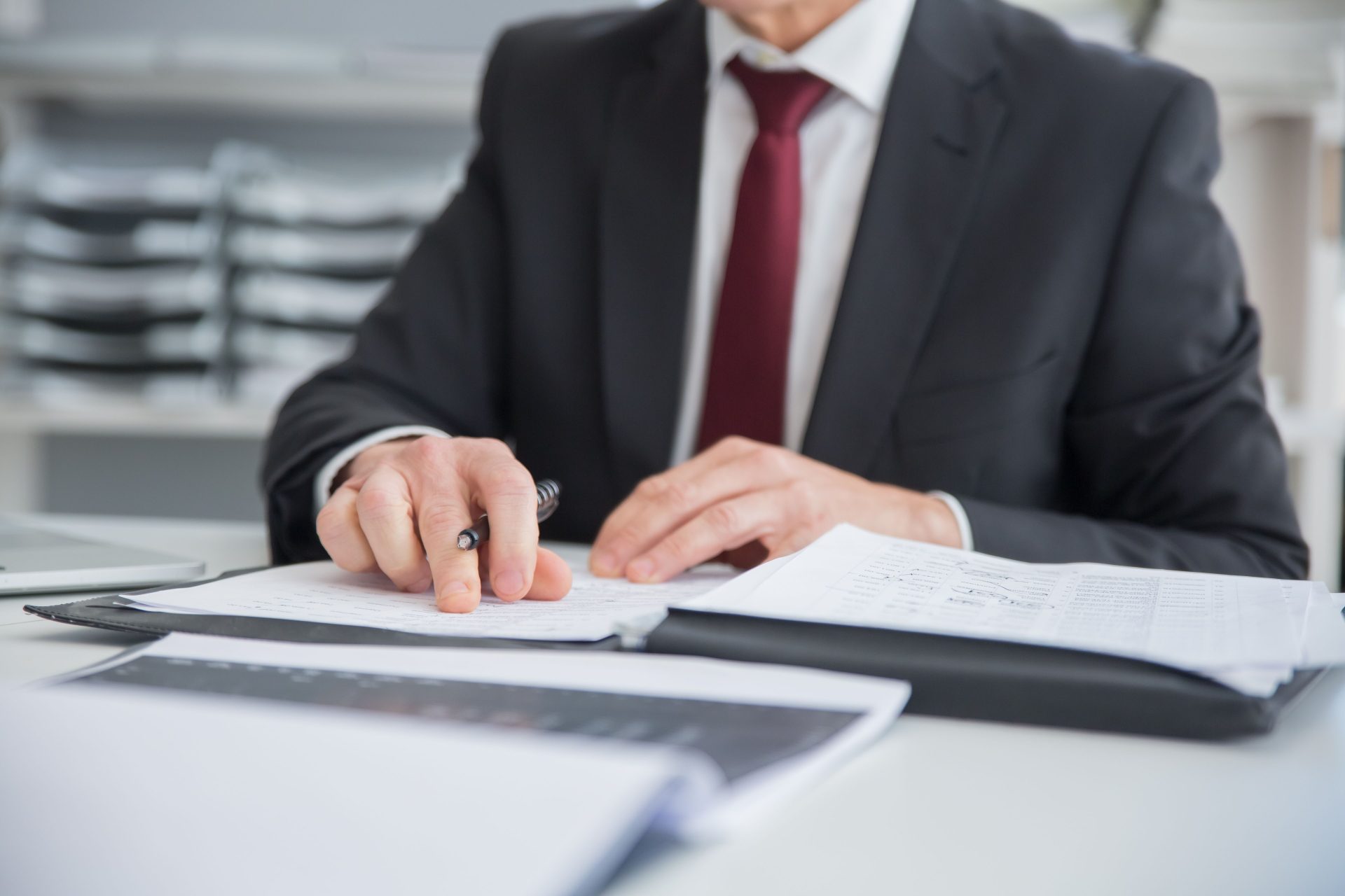Close-up of a businessman reviewing documents at an office desk. Focus on hands and paperwork.